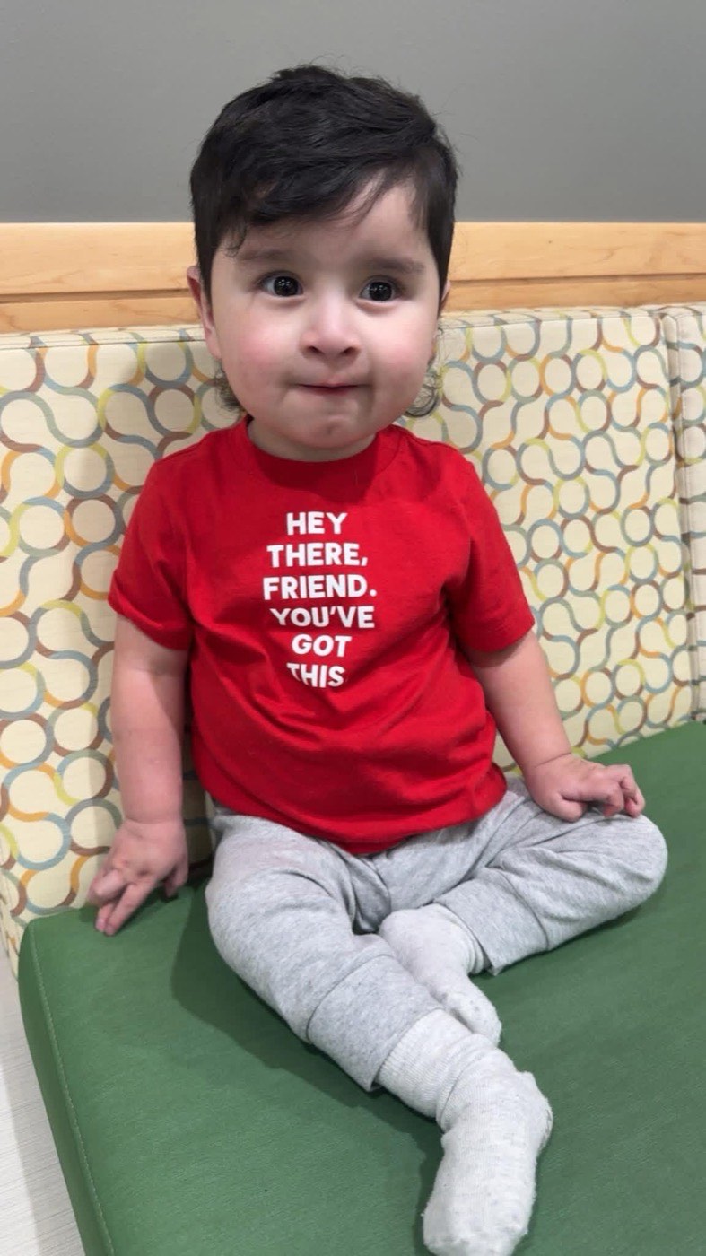 Damian sitting on a clinic exam bench in a red t-shirt that reads "Hey there, friend. You've got this."